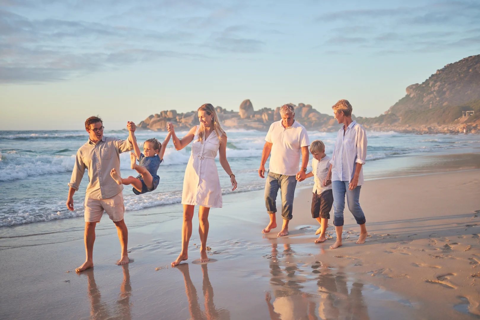 Multigenerational family enjoying a walk on the beach at sunset, an example of family tourism and intergenerational travel.