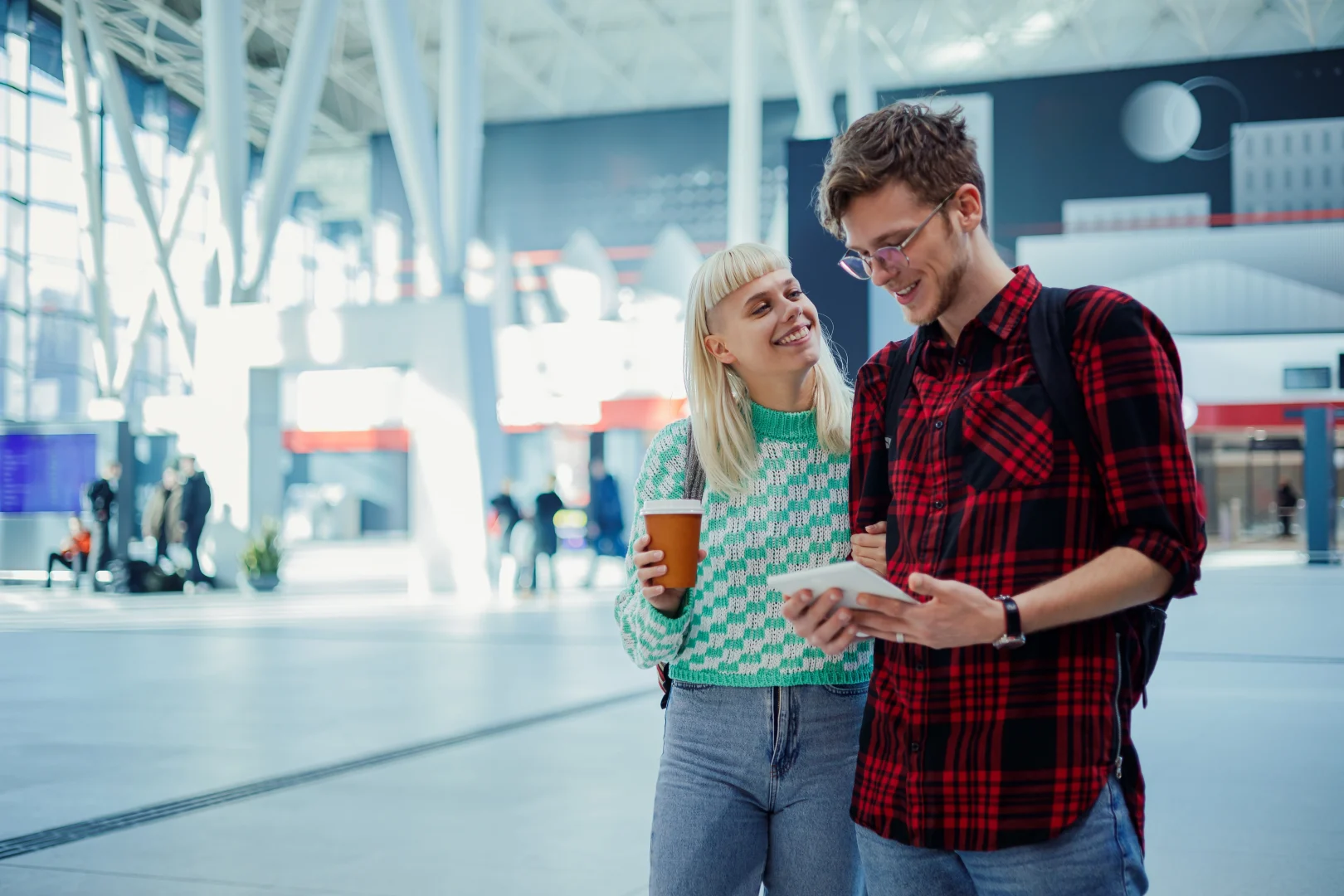 Young Generation Z couple consulting their trip on their cell phone at a modern airport, an example of digital and connected tourism.